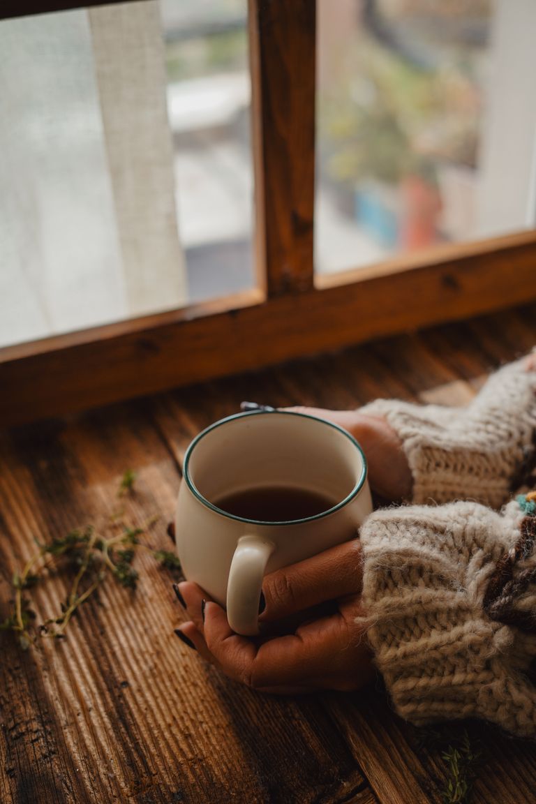 A person holding a coffee mug by a rustic window, creating a warm and cozy ambience.